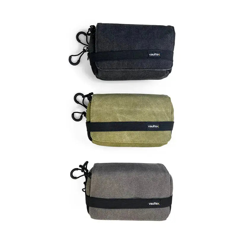 Three small rectangular pouches or cases shown vertically on a white background, each in a different color: dark charcoal gray, olive green, and heather gray. Each item has a black strap across the front with a small white 'vaultlax' logo and a black carabiner clip on the side.