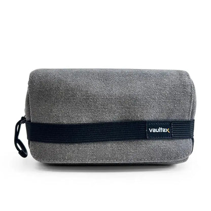 A gray textured canvas pouch with a black elastic band and a small 'Vaultlax' logo patch, shown on a clean white background.